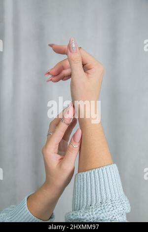 Frauenhände mit schöner Maniküre und Ringen sind in einer schönen, sanften, eleganten Geste gefaltet Stockfoto