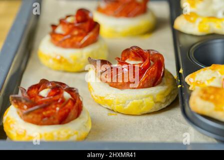 Frisches, hausgemachtes Gebäck. Mischung aus Blätterteig und Vorspeisen. Rosafarbter Pfefferoni-Kuchen. Gebäck mit Salami. Stockfoto