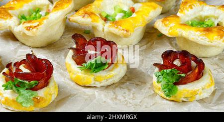 Frisches, hausgemachtes Gebäck. Mischung aus Blätterteig und Vorspeisen. Rosafarbter Pfefferoni-Kuchen. Gebäck mit Salami. Stockfoto