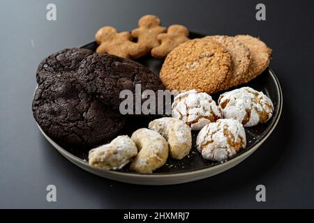 Hausgemachte Schokoladenkekse mit Haferflocken, die auf einem schwarzen Hintergrund auf einem schwarzen Teller mit Zucker bestreut wurden Stockfoto