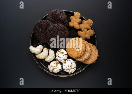 Hausgemachte Schokoladenkekse mit Haferflocken, die auf einem schwarzen Hintergrund auf einem schwarzen Teller mit Zucker bestreut wurden Stockfoto