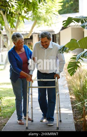 Selbst der kleinste Schritt ist immer noch ein Fortschritt. Aufnahme einer älteren Frau, die ihrem Mann bei der Anpassung an seinen neuen Wanderer hilft. Stockfoto
