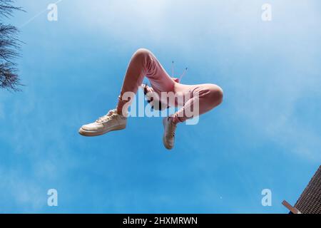 Junge schöne Frau in rosa Sportanzug springt voller Glück in einem freudigen Sprung in den blauen Himmel, kopieren Raum Stockfoto