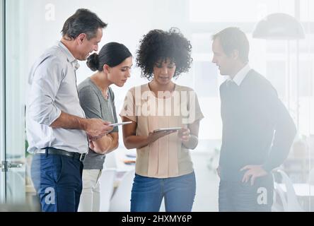 Technologische Teamarbeit. Aufnahme einer Gruppe von Kollegen, die gemeinsam ein digitales Tablet im Büro nutzen. Stockfoto