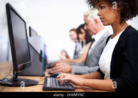 Hart arbeiten, um die Arbeit zu erledigen. Die Aufnahme einer attraktiven jungen Frau, die mit ihren Kollegen im Hintergrund am Schreibtisch arbeitet. Stockfoto