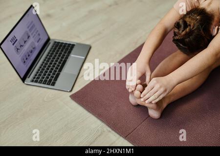 Draufsicht auf Teenager-Mädchen, die Stretching-Übungen machen, während sie Yoga zu Hause über Online-Unterricht genießen Stockfoto