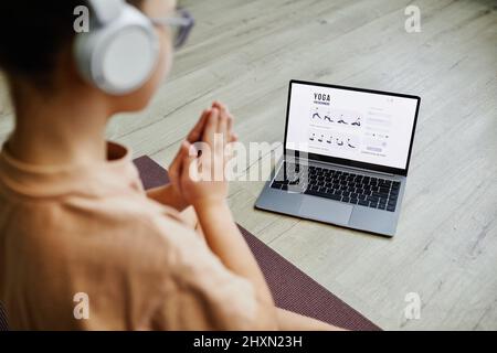 Über die Schulter schauen, wie das Kind den Online-Unterricht per Laptop ansieht, während es zu Hause Yoga praktiziert Stockfoto