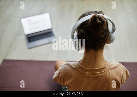 Aus der Ferne können Sie das Kind beobachten, während es sich den Online-Unterricht per Laptop ansieht, während es zu Hause Yoga praktiziert, Platz zum Kopieren Stockfoto