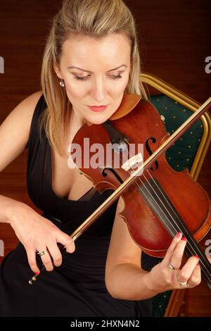 Beruhigt durch den Klang ihrer Saiten. Eine junge Frau, die sitzt und Geige spielt. Stockfoto
