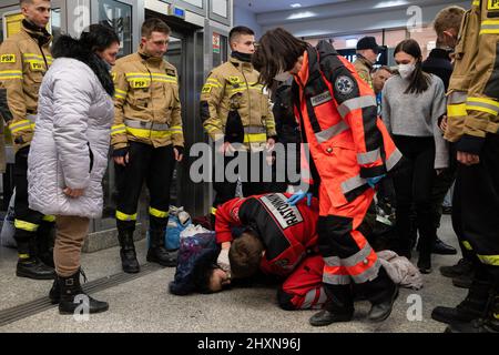 Kraków, Polen, 13/03/2022, Sanitäter sehen, wie sie eine Frau auf dem Boden liegen sehen. Flüchtlinge aus der Ukraine warten darauf, dass die Züge nach Westeuropa fahren. Kredit: SOPA Images Limited/Alamy Live Nachrichten Stockfoto