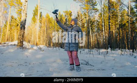 Frau, die auf einem Handheld-Film hält 3-Achsen-Gimbal-Stabilisiergerät im Winter für Smartphone. Girl Blogger Make Selfie, Broadcast Video Blogging, Vlogging. Videograf Operator Nimmt Fotovideo Auf. Stockfoto