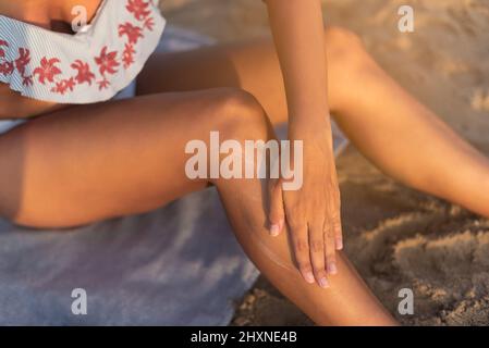 Crop Frau Anwendung Creme auf Bein am Strand Stockfoto