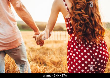 Nahaufnahme der Hände eines Paares, die sich gegenseitig halten, während sie durch das Weizenfeld gehen, und der Freund, der seine Freundin an einen geheimen Ort bringt, er Stockfoto