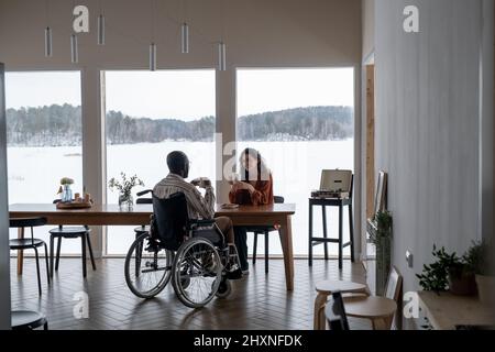 Glücklich junge interracial Paar reden und mit Tee am Tisch im Wohnzimmer oder geräumige Küche der modernen Wohnung Stockfoto