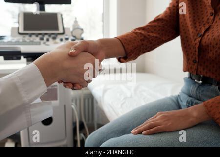 Handschlag einer jungen Ärztin und Patientin, die nach einer medizinischen Untersuchung gegen Ultraschallgeräte sitzt Stockfoto