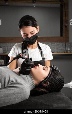 Dauerhaftes Make-up. Spa Schönheitsbehandlungen. Junge Frau. Der Meister legt das Tattoo auf die Lippen. Professionelle Microblading im Gesicht. Weibliche Kosmetologie Stockfoto