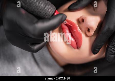 Nahaufnahme von geschwollenen weiblichen Lippen während der Anwendung von Permanent Make-up. Tattoo auf dem Gesicht und Mikropigmentierung der Lippen. Professionelle Gesichtsbehandlung Stockfoto