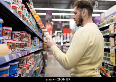 Ein männlicher Käufer in einem Baumarkt wählt Farbe für Innen- und Außenlackierungen Stockfoto