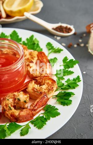 Gegrillte Garnelen auf weißem Teller mit frischer Petersilie, Gewürzen und Zitrone, gebratene Garnelen mit Sauce im Glas Stockfoto