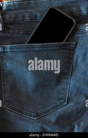 Der obere Teil einer alten schwarzen Jeans und ein Smartphone mit schwarzem Bildschirm Stockfoto