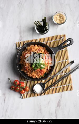 Hausgemachter gebratener Kimchi-Reis mit grüner Zwiebel, Nori und Sesamsamen auf einer Pfanne, Blick von oben auf dem Marmortisch Stockfoto