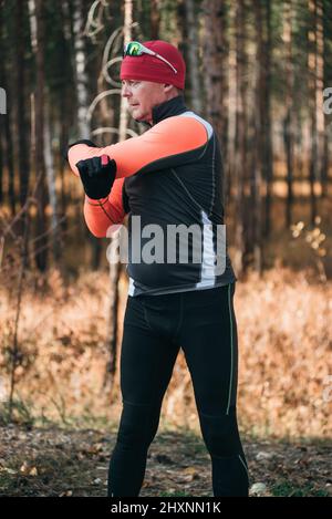 Training eines Athleten auf den Rollern. Biathlon-Fahrt auf den Rollskiern mit Skistöcken, im Helm. Herbsttraining. Rollensport. Erwachsener Mann, der auf Schlittschuhe reitet. Der Athlet macht das Training. Stockfoto