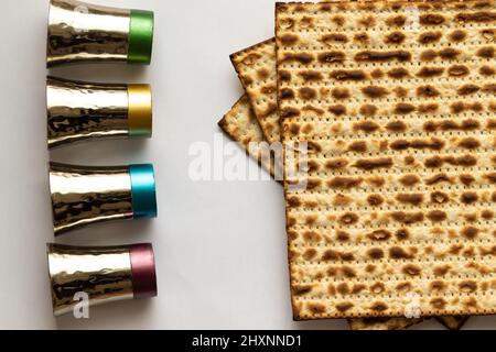 Drei Matzahs - Jüdisches Brot für Passah. Neben vier kleinen silbernen Tassen. Weißer Hintergrund Stockfoto