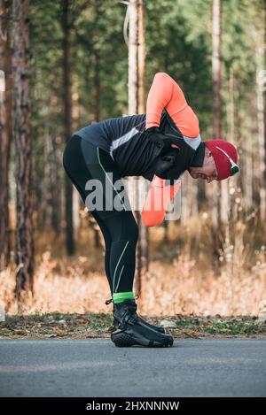 Training eines Athleten auf den Rollern. Biathlon-Fahrt auf den Rollskiern mit Skistöcken, im Helm. Herbsttraining. Rollensport. Erwachsener Mann, der auf Schlittschuhe reitet. Der Athlet macht das Training. Stockfoto