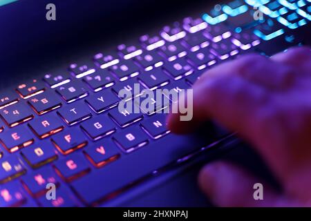 Arbeiten an einer Neon-Computertastatur mit farbiger Hintergrundbeleuchtung. Computer-Videospiele, Hacking, Technologie, Internet-Konzept. Ausgewählter Fokus. Hochwertige Fotos Stockfoto