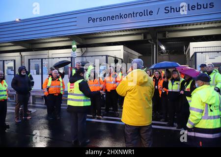 Köln, Deutschland. 14. März 2022. Streikende Fluggastkontrollmitarbeiter versammelten sich im Regen an einer Bushaltestelle. Die Gewerkschaft Verdi hat das Sicherheitspersonal bei der Passagierkontrolle an mehreren deutschen Flughäfen aufgefordert, am Montag ganztägige Warnstreiks zu starten. Sie sind Teil des Lohnstreits zwischen Verdi und dem Bundesverband der Luftfahrtunternehmen (BDLS). Die Gewerkschaft verhandelt derzeit über einen neuen Tarifvertrag mit dem Arbeitgeberverband für rund 25.000 Sicherheitspersonal im ganzen Land. Quelle: Sascha Thelen/dpa/Alamy Live News Stockfoto