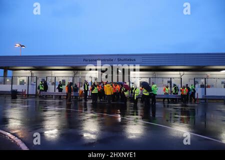 Köln, Deutschland. 14. März 2022. Streikende Fluggastkontrollmitarbeiter versammelten sich im Regen an einer Bushaltestelle. Die Gewerkschaft Verdi hat das Sicherheitspersonal bei der Passagierkontrolle an mehreren deutschen Flughäfen aufgefordert, am Montag ganztägige Warnstreiks zu starten. Sie sind Teil des Lohnstreits zwischen Verdi und dem Bundesverband der Luftfahrtunternehmen (BDLS). Die Gewerkschaft verhandelt derzeit über einen neuen Tarifvertrag mit dem Arbeitgeberverband für rund 25.000 Sicherheitspersonal im ganzen Land. Quelle: Sascha Thelen/dpa/Alamy Live News Stockfoto