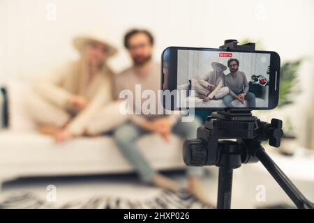 Das junge verheiratete kaukasische Paar, das Videos dreht und die Kamera in Innenräumen anschaut. Hochwertige Fotos Stockfoto