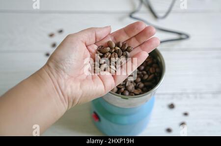 Frau Handfläche hält Kaffeebohnen mit elektrischer Mühle im Hintergrund. Stockfoto