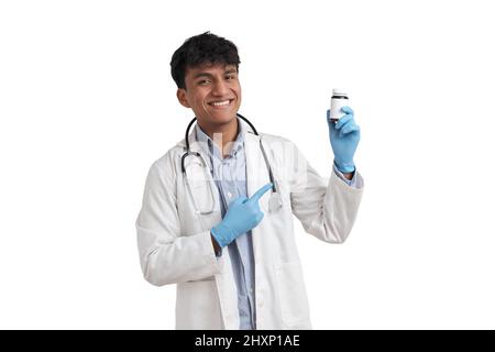 Junger peruanischer Arzt lächelt und zeigt isoliert auf eine Pillenflasche. Stockfoto