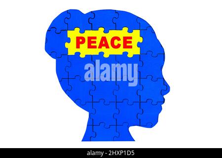 Silhouette eines weiblichen Kopfprofils aus hölzernen Puzzleteilen, die blau und gelb lackiert sind und Frieden lesen. Stockfoto