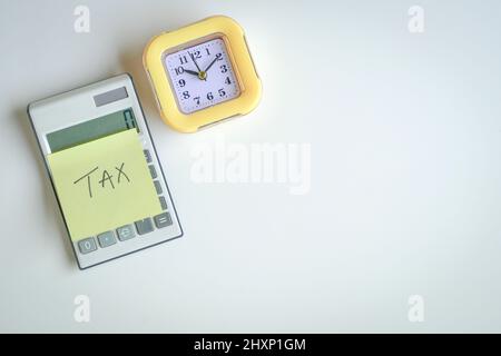 Das Wort Tax auf gelbem Klebepapier, kleben Sie auf den Rechner neben eine gelbe Uhr. Draufsicht. Konzept der Steueranmeldung. Stockfoto