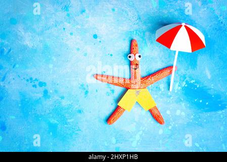 Fröhlicher roter Seesterne-Charakter, der auf hellblauem Hintergrund mit einem Sonnenschirm in der Hand schwimmt. Kreatives Konzept für einen Urlaub am Meer. Stockfoto
