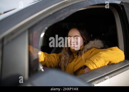 Junge Frau mit Down-Syndrom fährt ein Auto und lächelt. Stockfoto