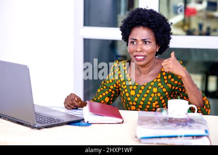 Schöne reife Geschäftsfrau in traditioneller Kleidung sitzt am Schreibtisch und redet unglücklich. Stockfoto