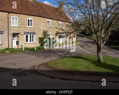 Eine Terrasse aus Steinhäusern mit Blick auf ein kleines Grün im hübschen Dorf Yardley Hastings, Northamptonshire, Großbritannien Stockfoto
