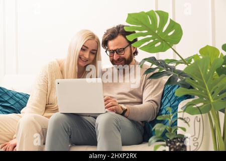 Junges kaukasisches Paar, das mit einem Laptop auf dem Sofa zusammenarbeitet Fernarbeit mittlere Aufnahme. Hochwertige Fotos Stockfoto