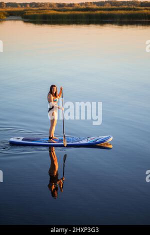 Porträt von oben einer kaukasischen Frau mittleren Alters, die am Abend im Sommer auf dem See schwattert und mit Schilf im Hintergrund lächelnd auf die Kamera blickt Stockfoto