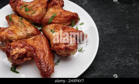 Gegrillte Hähnchenflügel auf einem Teller, auf dunklem Hintergrund Stockfoto
