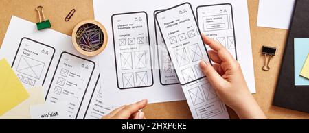 Web-Produkt-Designer arbeitet an mobilen responsive Website Konzept Banner. Flaches Bild mehrerer App-Drahtgardeskizzen über dem Schreibtisch des Produktdesigners. Stockfoto