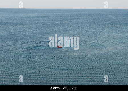 Kleines rotes Boot mit zwei Fischern auf blauem Meer mit Horizontlinie Stockfoto
