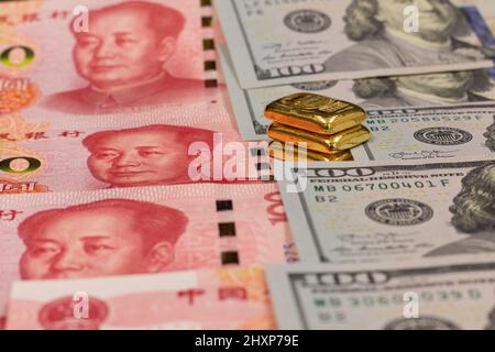 Stapel von reinen Goldbarren, Goldbarren, Barren auf dem Hintergrund von Renminbi oder RMB, CNY, Währung von China und US-Dollar-Banknoten Stockfoto
