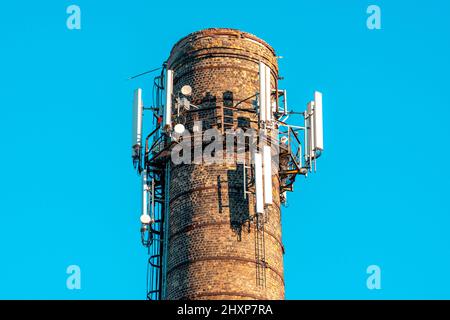 5G Antennen auf einem Ziegelrohr gegen einen klaren Himmel. Mobilfunk- und Internet-Antennen am Ziegelrohr des Kesselraums. Stockfoto