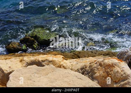 An einem sonnigen Tag treffen kleine Wellen auf nasse Felsen am Meer Stockfoto