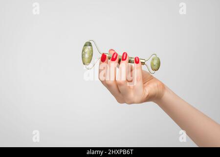 Kosmetische Jaderolle in der Hand einer Frau, roter Nagellack auf den Nägeln Stockfoto