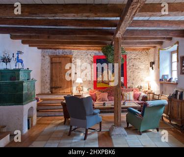 Wohnzimmer des Landhauses mit Holzbalken, grünem Kachelofen, Sesseln, Sofa und Gemälden Stockfoto